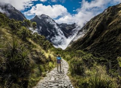 Hiker on a stone Inca path through a green Andean valley with misty peaks