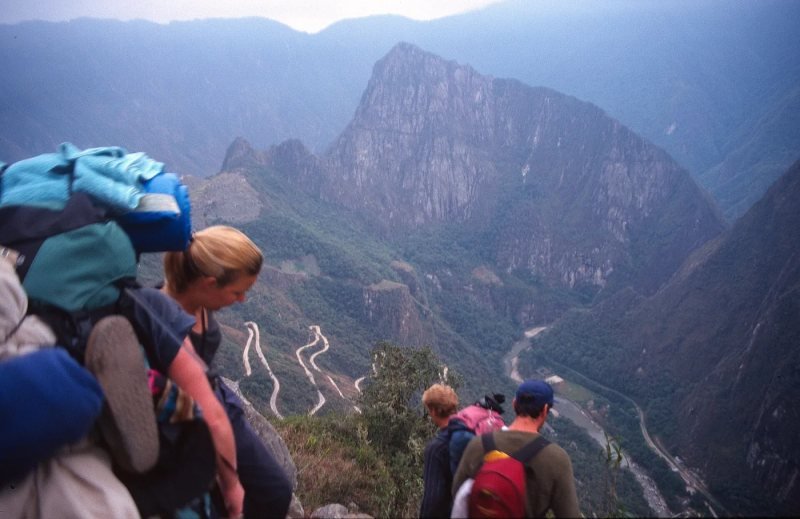 Hikers climbing stone steps on the Inca Trail with green peaks and cloud behind them