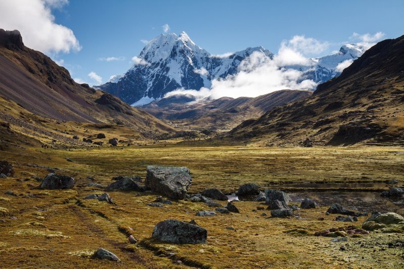 Snow-covered Ausangate above a golden grassland valley with boulders