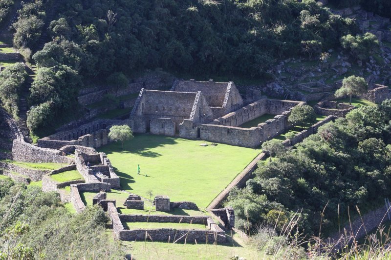 Stone terraces and buildings of Choquequirao on a green ridge with cloud-covered mountains behind