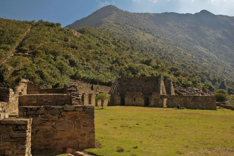 Two-story Inca buildings beside a grassy plaza at Choquequirao