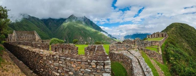 Stone buildings of Choquequirao with green mountains and clouds behind
