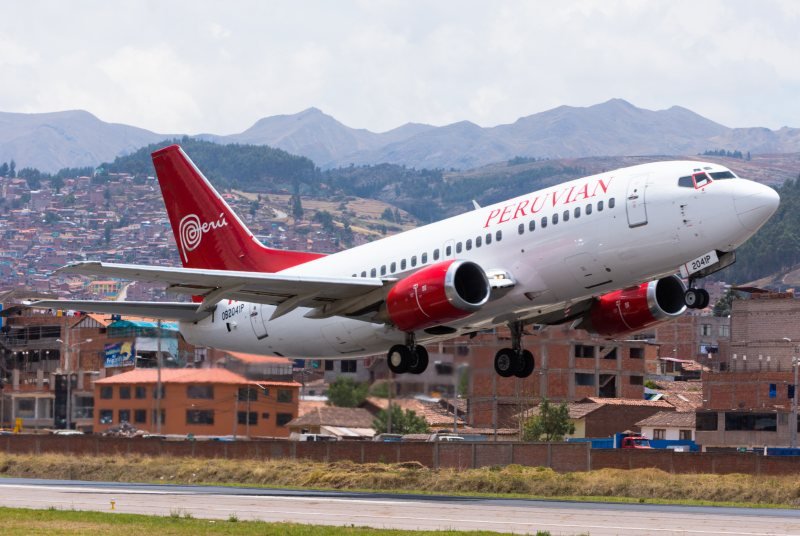 Passenger jet taking off from Cusco airport with the city rooftops and the surrounding hills behind