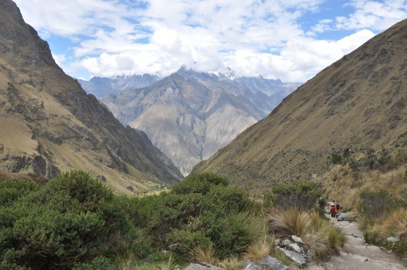 Stone trail climbing a valley toward Dead Woman's Pass, with snowy peaks behind