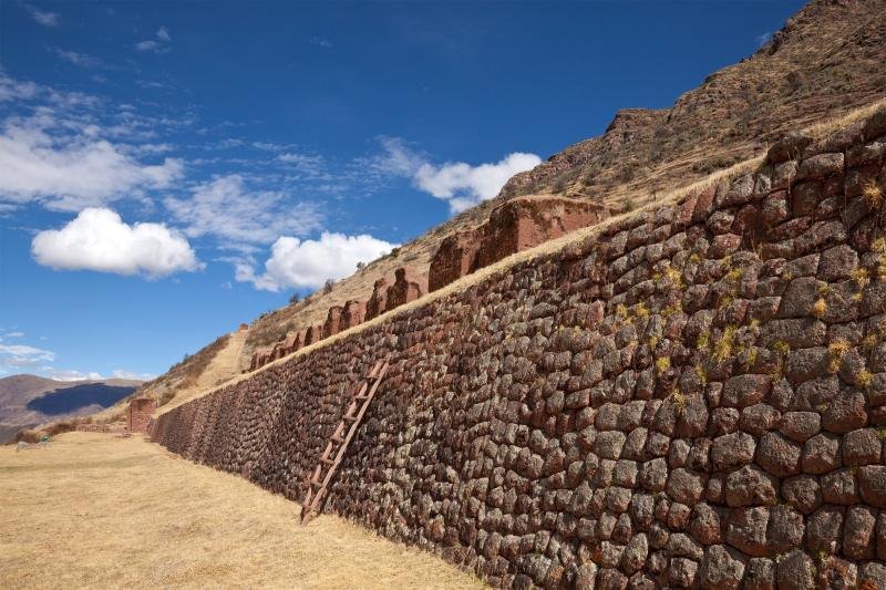 Long Inca retaining wall at Huchuy Qosqo under a blue sky