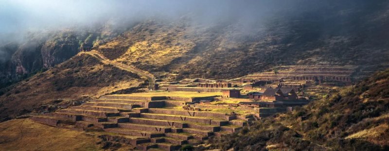Terraces and buildings of Huchuy Qosqo under clouds on the plateau