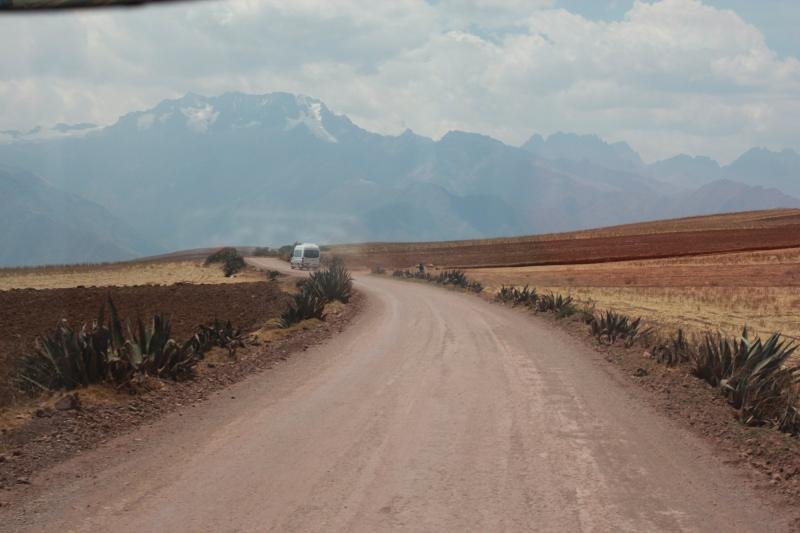 Dirt road to Moray across the red fields of the plateau, with the snowy Urubamba range behind