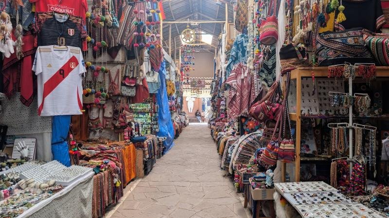 Textile and souvenir stalls along a covered lane at the Pisac craft market