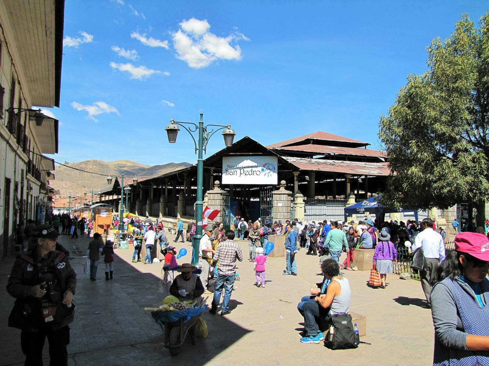 The street leading to the entrance of San Pedro market in Cusco, with shoppers a The street leading to the entrance of San Pedro market in Cusco, with shoppers and the market roof under a blue sky