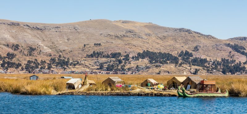 Uros floating island of golden totora reed with reed houses and a two-headed reed boat on Lake Titicaca