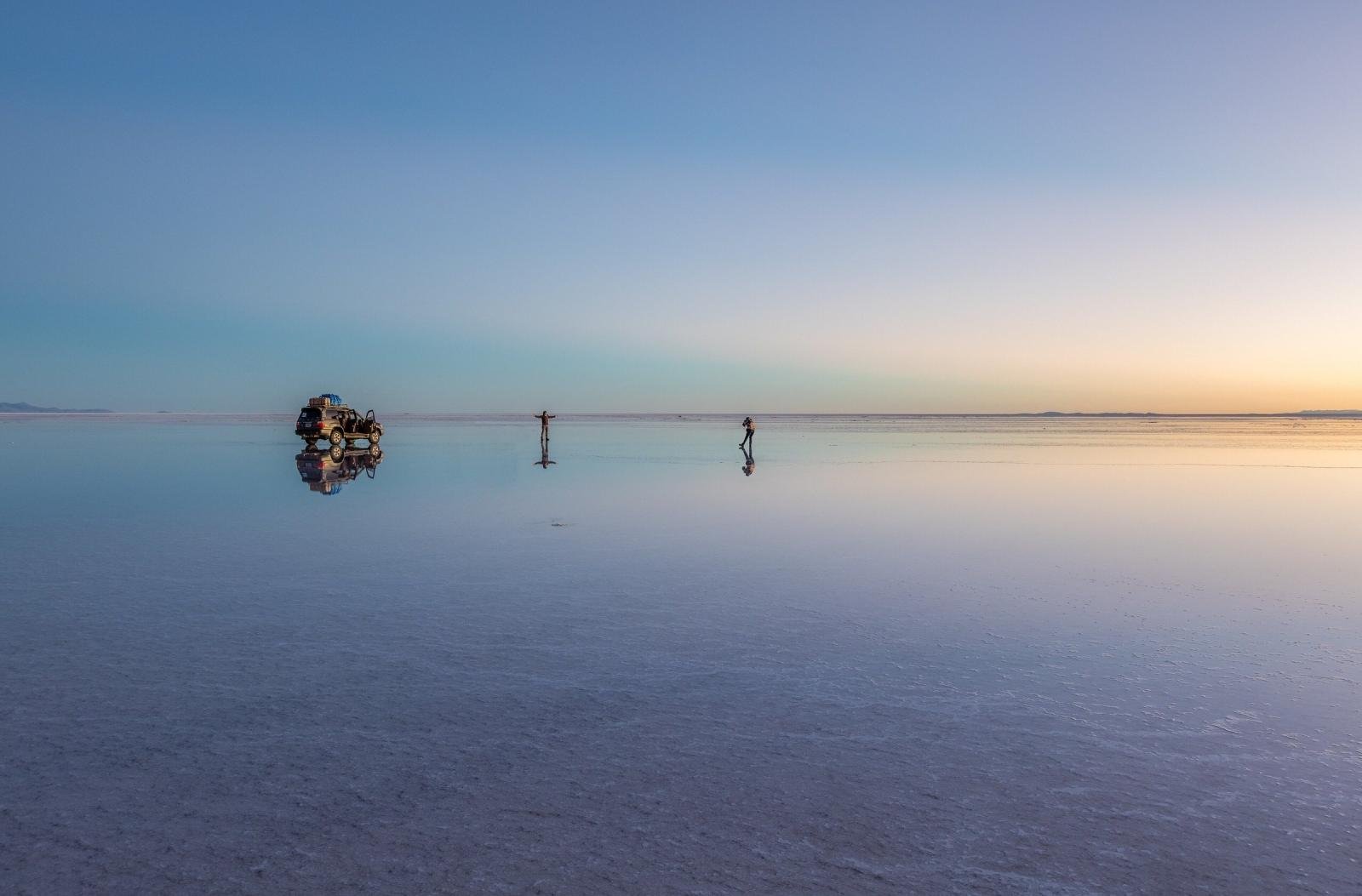 Vehicle and travelers reflected on the flooded Salar de Uyuni at sunset