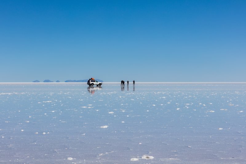 Jeep and travelers far out on the wet Salar de Uyuni under a clear blue sky