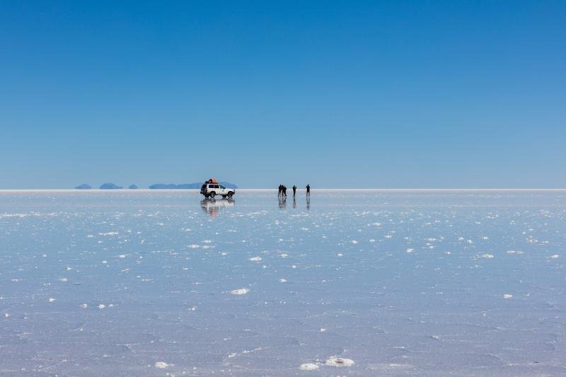 Salar de Uyuni Jeep and travelers far out on the wet Salar de Uyuni under a clear blue sky