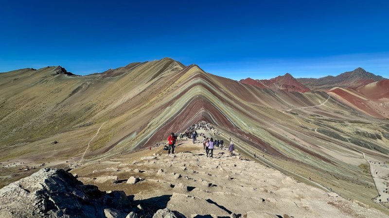 Hikers on the summit ridge of Vinicunca with its red, green and yellow mineral stripes