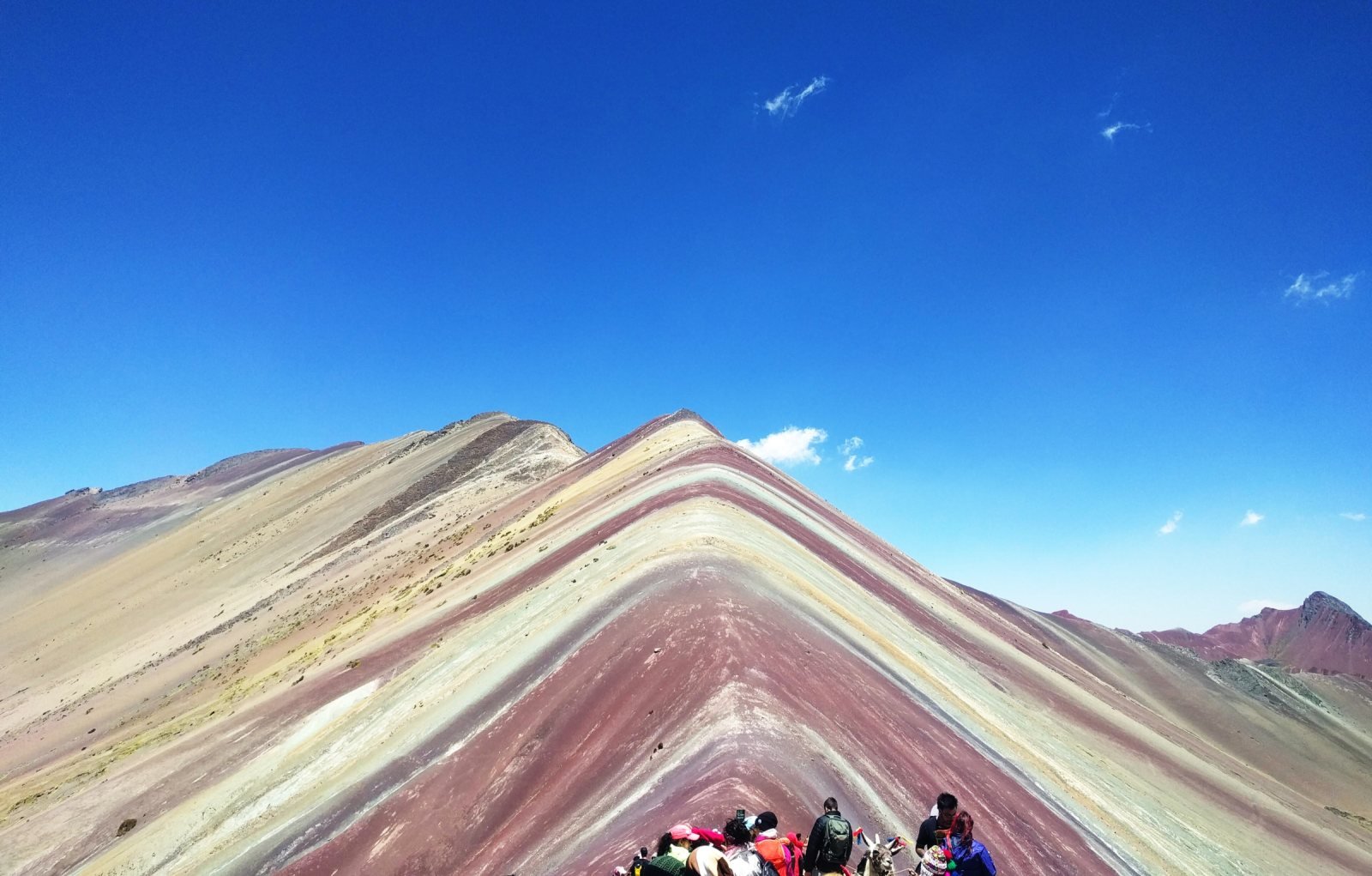 Striped slopes of Vinicunca under a deep blue sky with hikers at the viewpoint