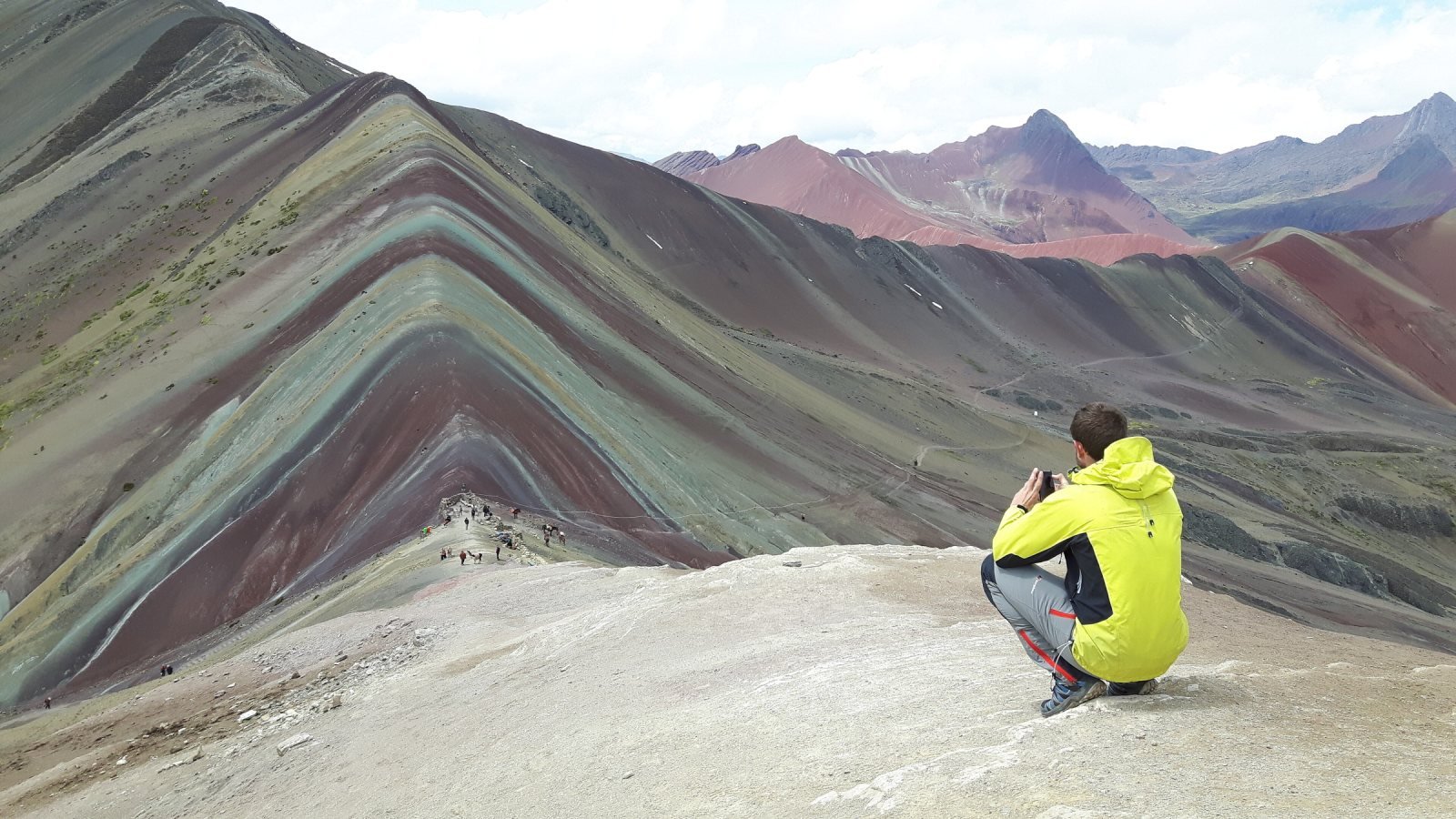 Hiker looking over the striped ridges of Vinicunca toward the Red Valley
