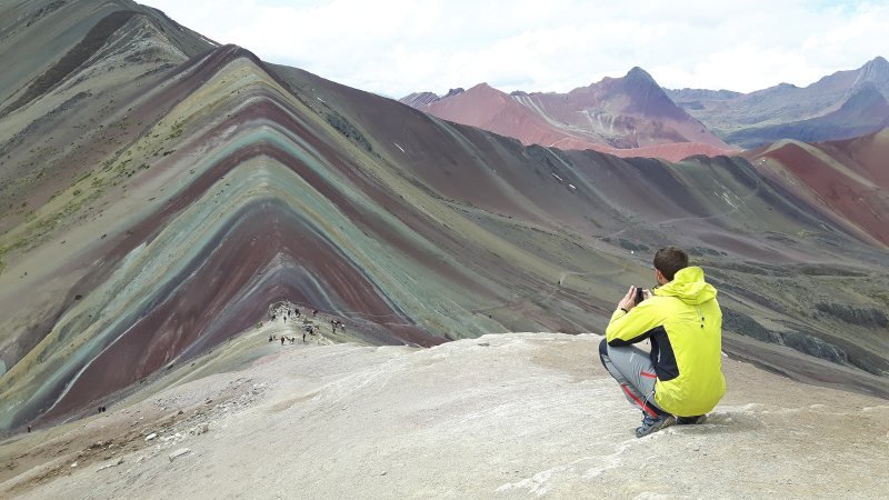 Hiker looking over the striped ridges of Vinicunca toward the Red Valley